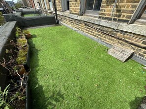 A small, enclosed outdoor area with artificial grass, a concrete edge, and a brick wall. - 1-Bedroom Flat in Islington! (Greater London)