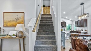 Una escalera que conduce a una zona de cocina con una mesa y sillas visibles al fondo.
