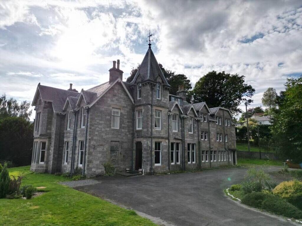 A large, historic stone building with multiple chimneys and a prominent tower.