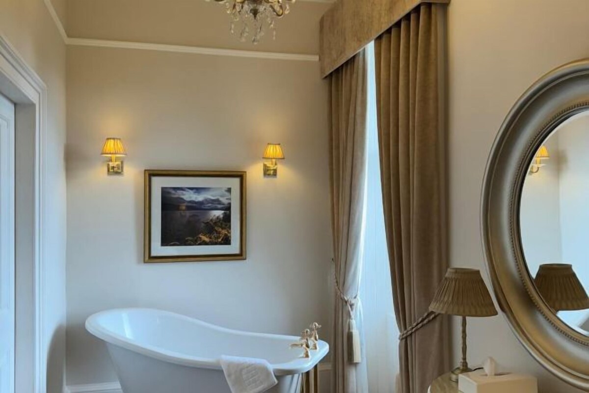 A bathroom with a freestanding bathtub, a framed picture on the wall, and a round mirror.