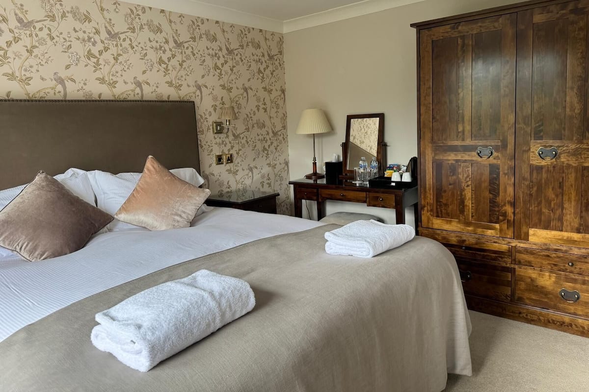 Una habitación de hotel con una cama grande, un armario de madera, una mesita de noche con lámpara y un espejo.