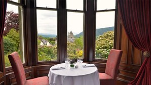 Mesa para dos personas con vistas a una iglesia y follaje verde a través de amplias ventanas.