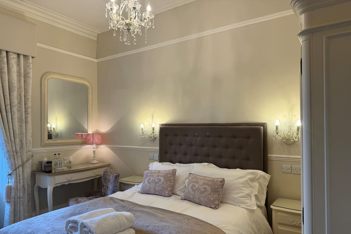 Un dormitorio elegante con una cama grande, un tocador, un espejo y una araña.