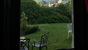 Vista a través de una ventana de un jardín exuberante con un arcoíris, una iglesia y una zona verde con sillas.