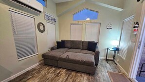 A cozy room with a sectional sofa, a skylight, and a small table with a lamp. - Modern Tiny Home Near Sequoia National Park (Lindsay)