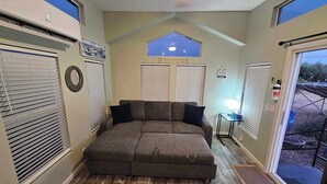 A cozy room with a sectional sofa, a ceiling fan, and a view through a door. - Modern Tiny Home Near Sequoia National Park (Lindsay)