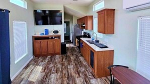 A compact kitchen with wooden cabinets, a microwave, and a large TV mounted on the wall. - Modern Tiny Home Near Sequoia National Park (Lindsay)