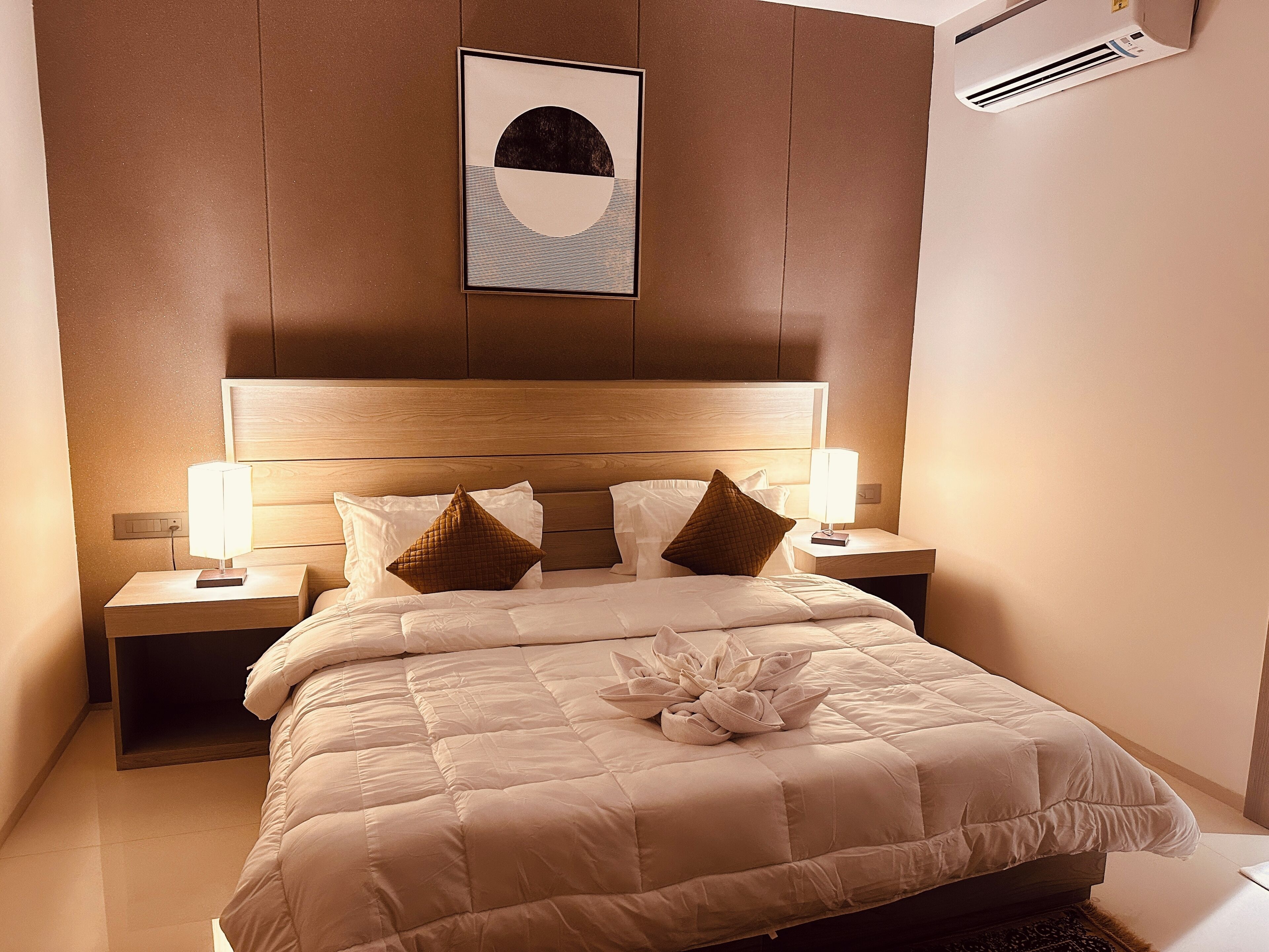 Ein Hotelzimmer mit einem großen Bett, zwei Nachttischen mit Lampen, einer Wandklimaanlage und einem gerahmten Kunstwerk über dem Bett.