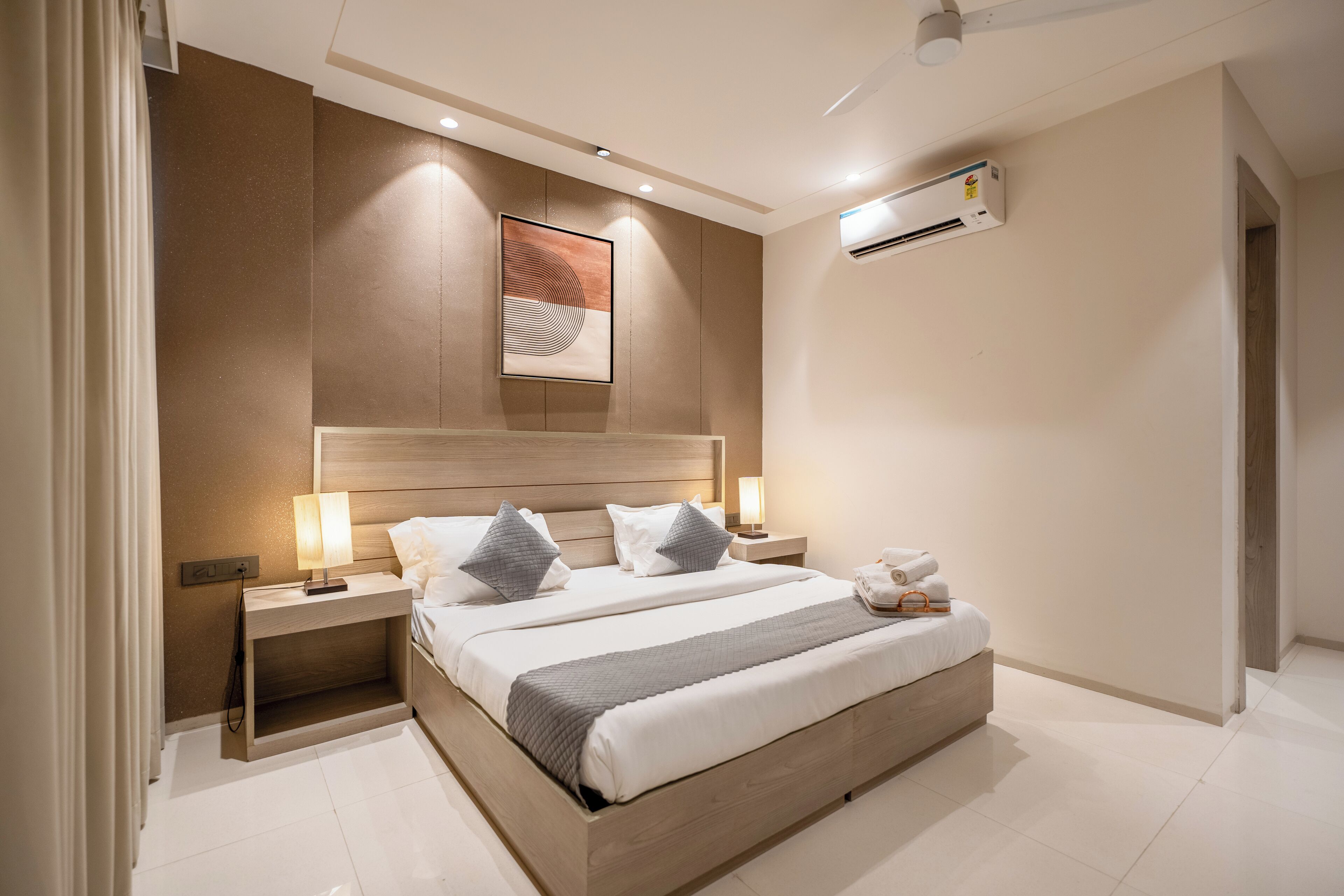 Una habitación de hotel moderna con una cama grande, lámparas de noche, aire acondicionado de pared y una obra de arte enmarcada sobre la cama.