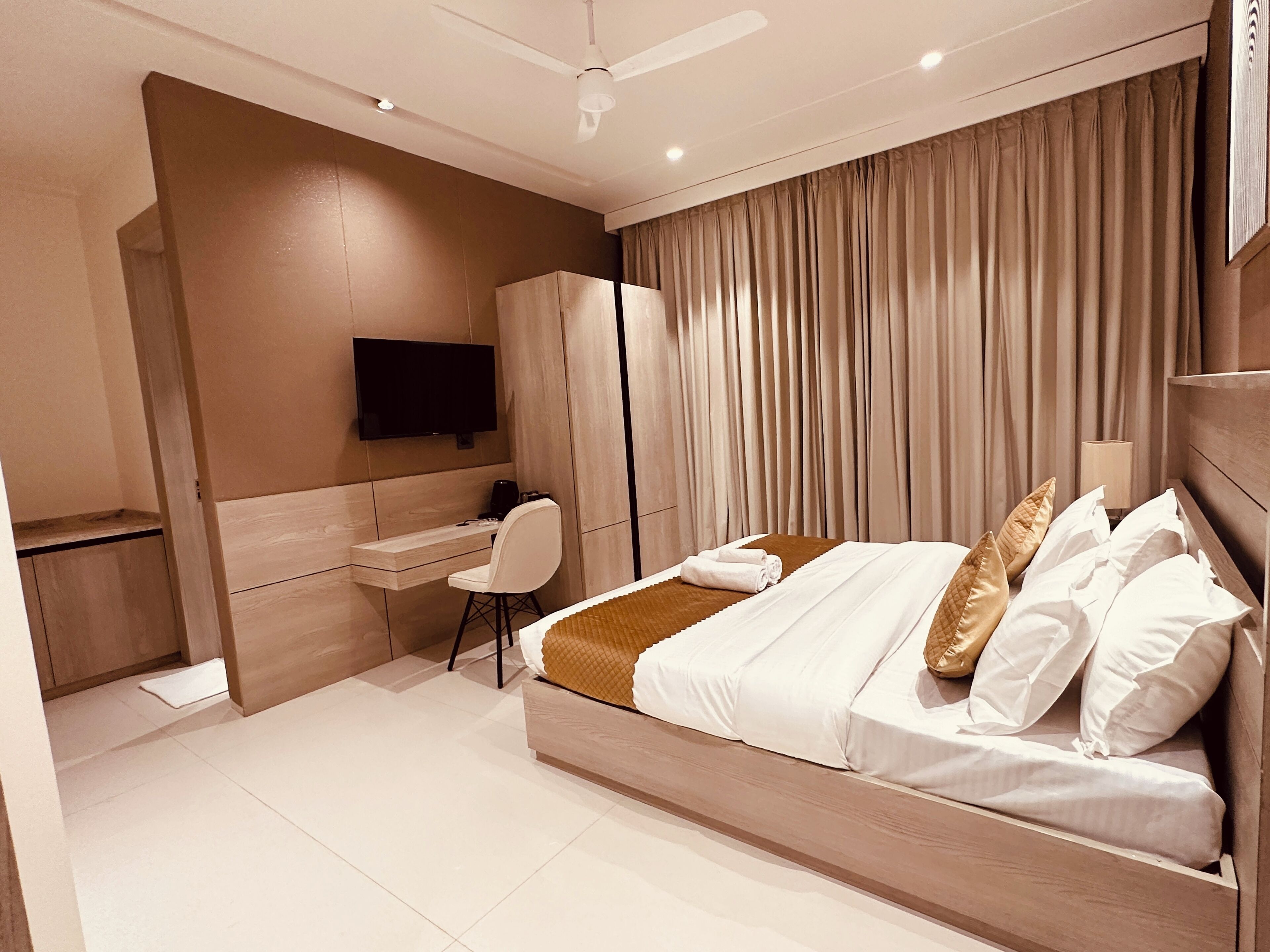 A modern hotel room with a bed, a desk, a chair, a television, and a large window with curtains.
