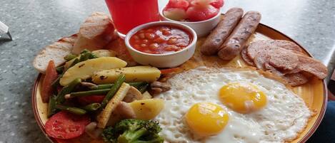 A plate of breakfast food including eggs, sausages, toast, and a glass of red drink.