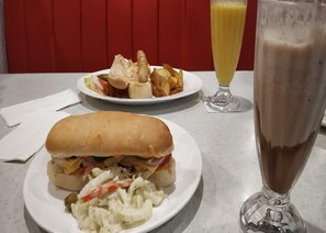 A meal consisting of a sandwich, potato chips, and a glass of a yellow beverage on a table. - The Lodgers Luxury Hotel Near GolfCourse (Gurugram)