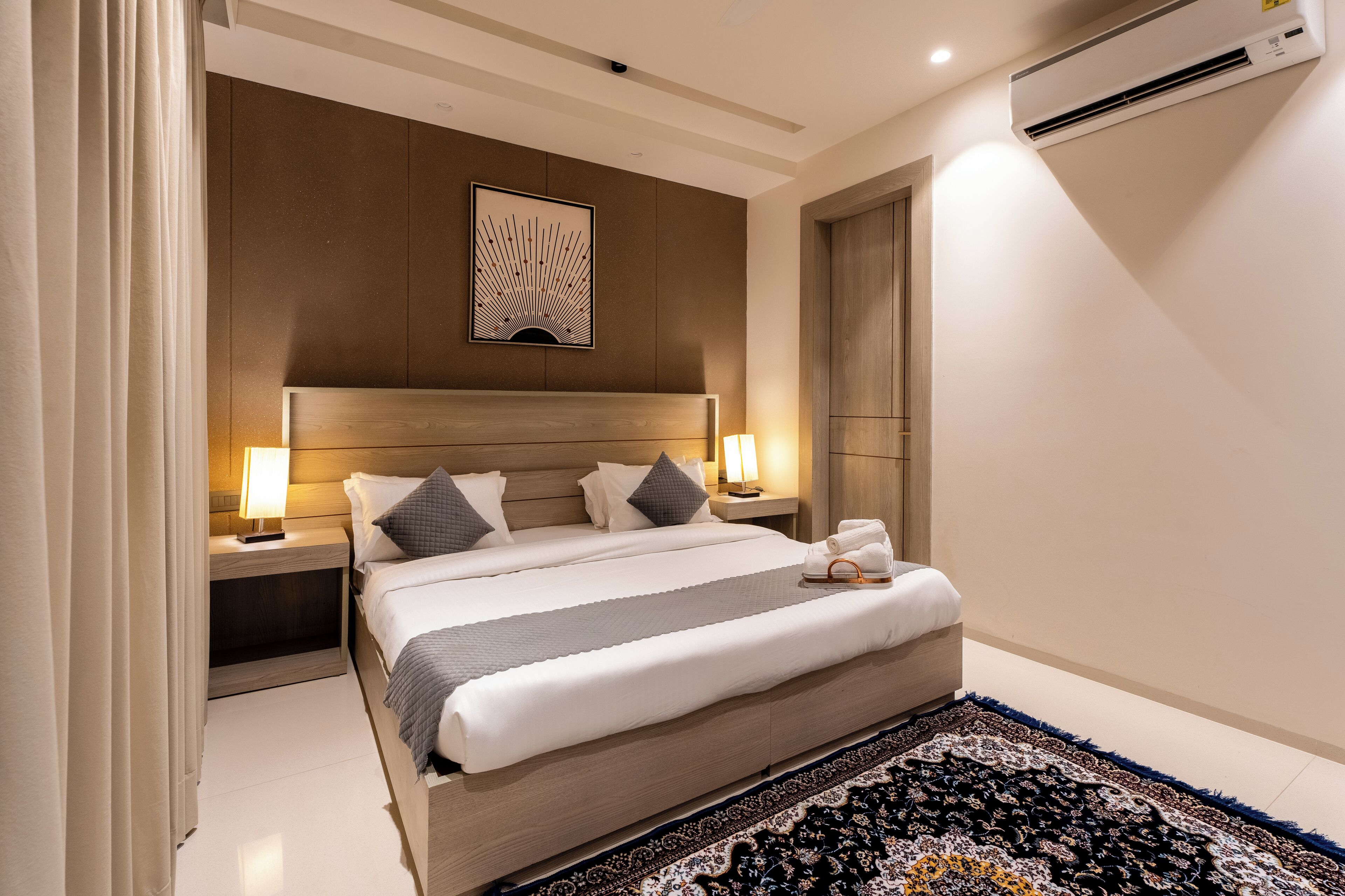 Une chambre d’hôtel moderne avec un grand lit, des lampes de chevet, un climatiseur fixé au mur et un tapis à motifs.