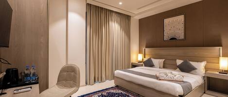 Une chambre d’hôtel moderne équipée d’un lit, de tables de chevet, d’une chaise, d’un bureau avec une télécommande et d’un tapis décoratif.