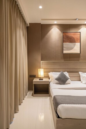A modern hotel room with a neatly made bed, a bedside table with a lamp, and a large abstract painting on the wall. - The Lodgers Luxury Hotel Near GolfCourse (Gurugram)