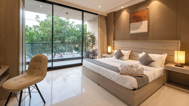 A modern bedroom with a large bed, bedside lamps, a chair, and a view of greenery outside.