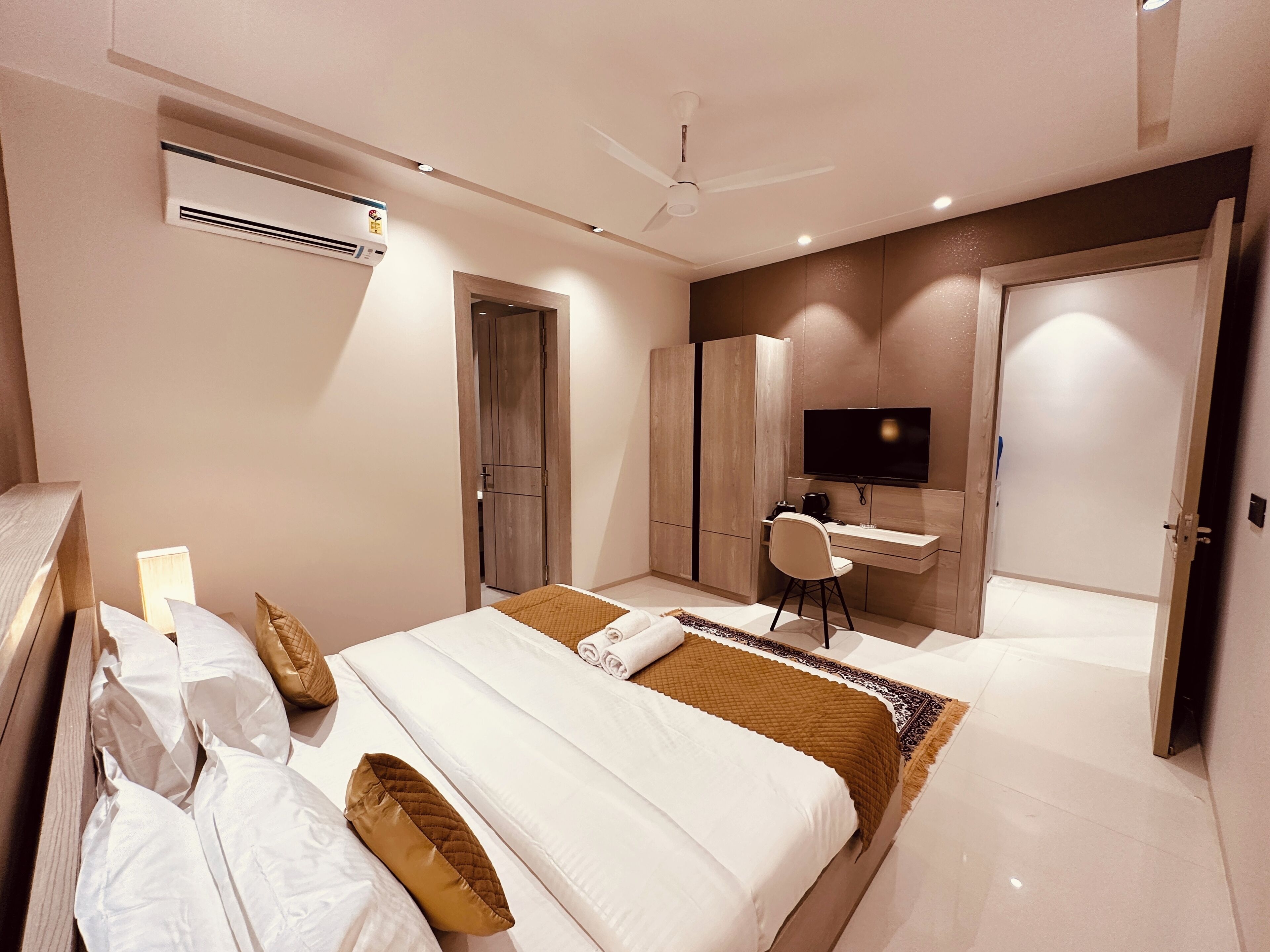 A modern bedroom with a bed, a desk, a chair, a television, and a wardrobe.