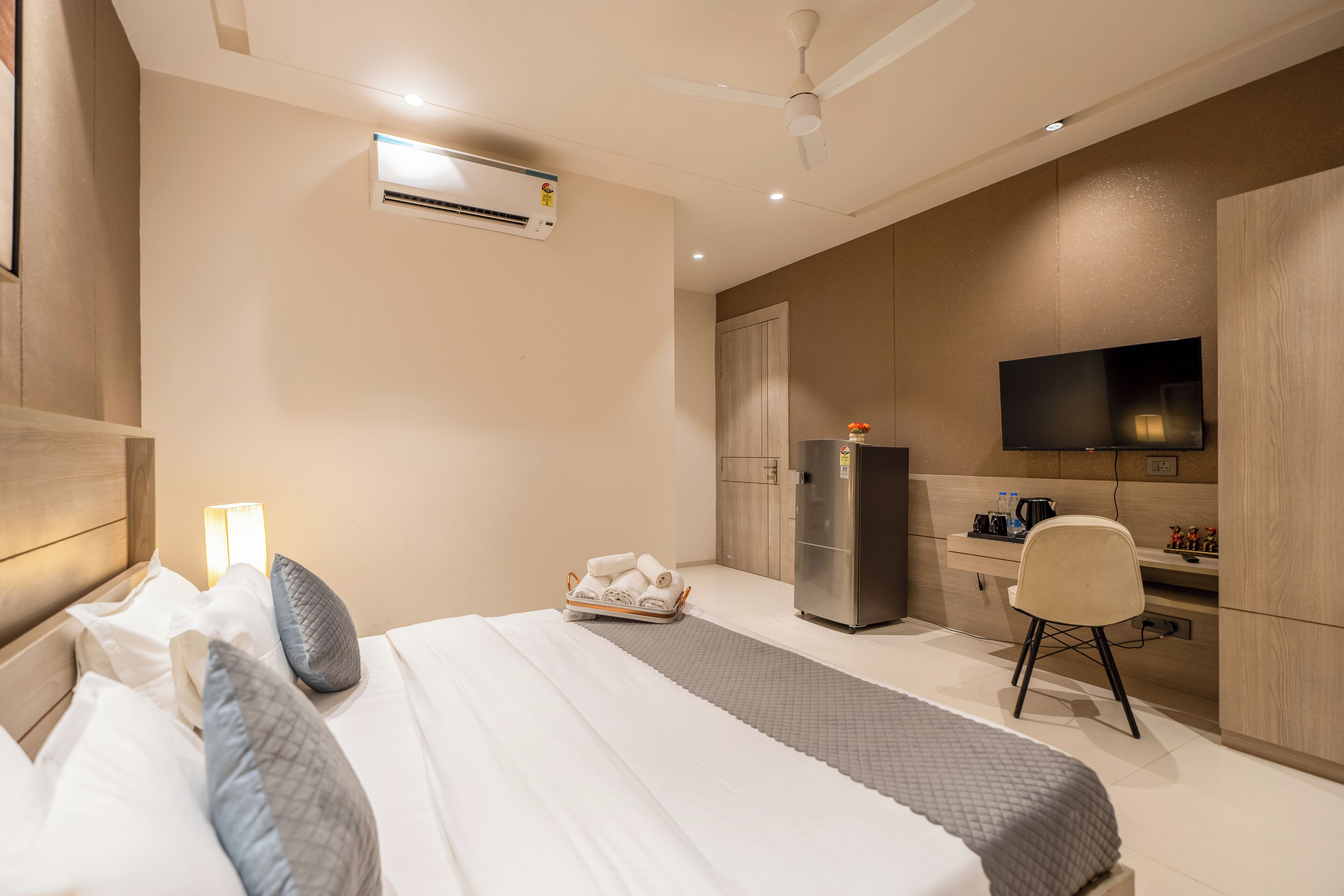 A hotel room with a bed, a desk, a chair, a television, and a refrigerator.