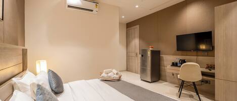 A hotel room with a bed, a desk, a chair, a television, and a refrigerator.