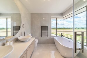 Een moderne badkamer met een groot bad, twee wastafels, een toilet en een grote spiegel.