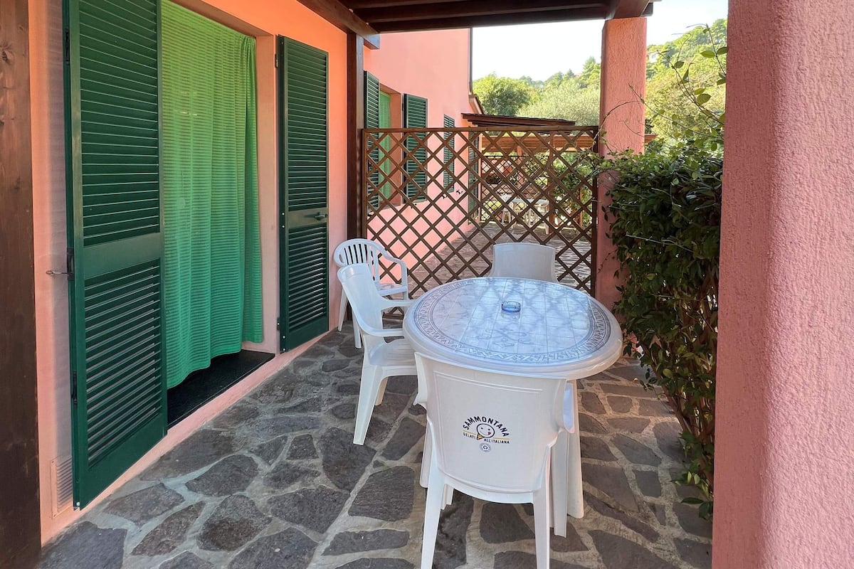 A covered patio with a stone floor, a round table, and two white chairs.