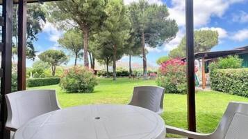 Une terrasse couverte, dotée d’une table ronde et de quatre chaises, qui offre une vue sur un jardin bien entretenu, agrémenté d’arbres et d’arbustes.