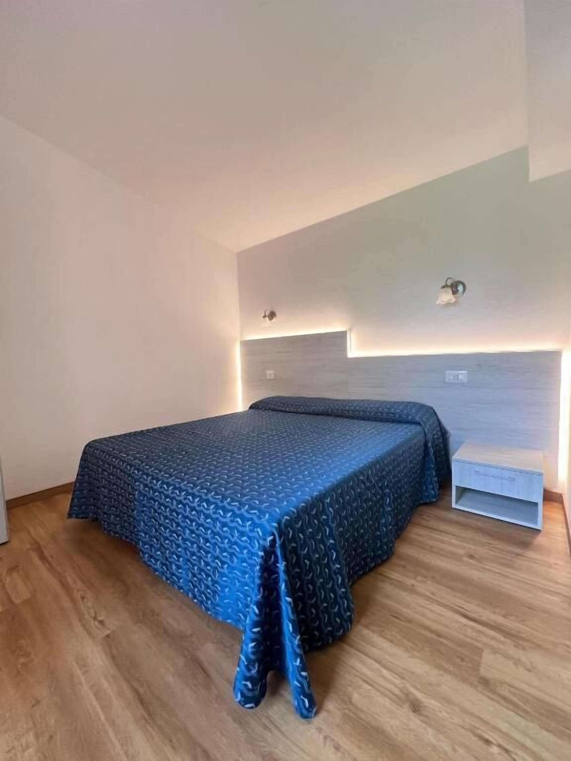 Een slaapkamer met een bed, nachtkastje en een wandlamp.