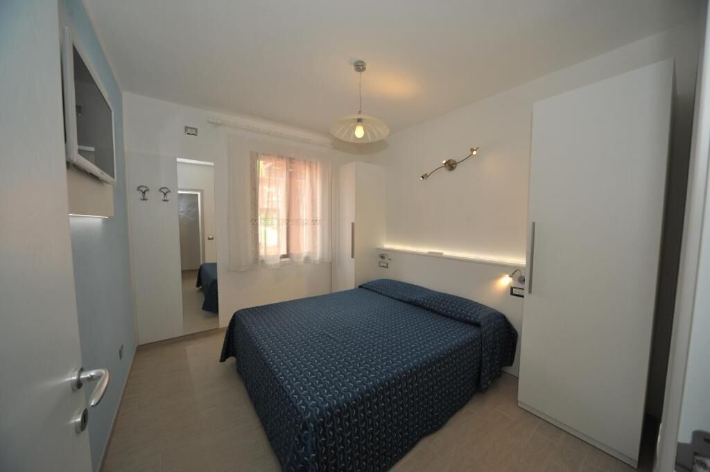 Um quarto com uma cama, uma porta, um espelho e uma janela com cortinas.