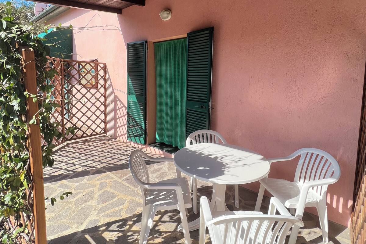A covered patio with a table and chairs, a wooden fence, and a green curtain.