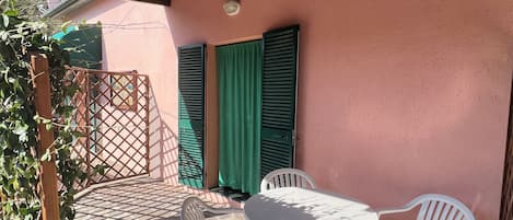 A covered patio with a table and chairs, a wooden fence, and a green curtain.