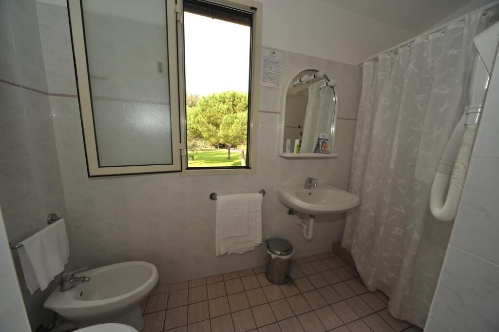 A bathroom with a toilet, bidet, sink, and a window with a view of trees.