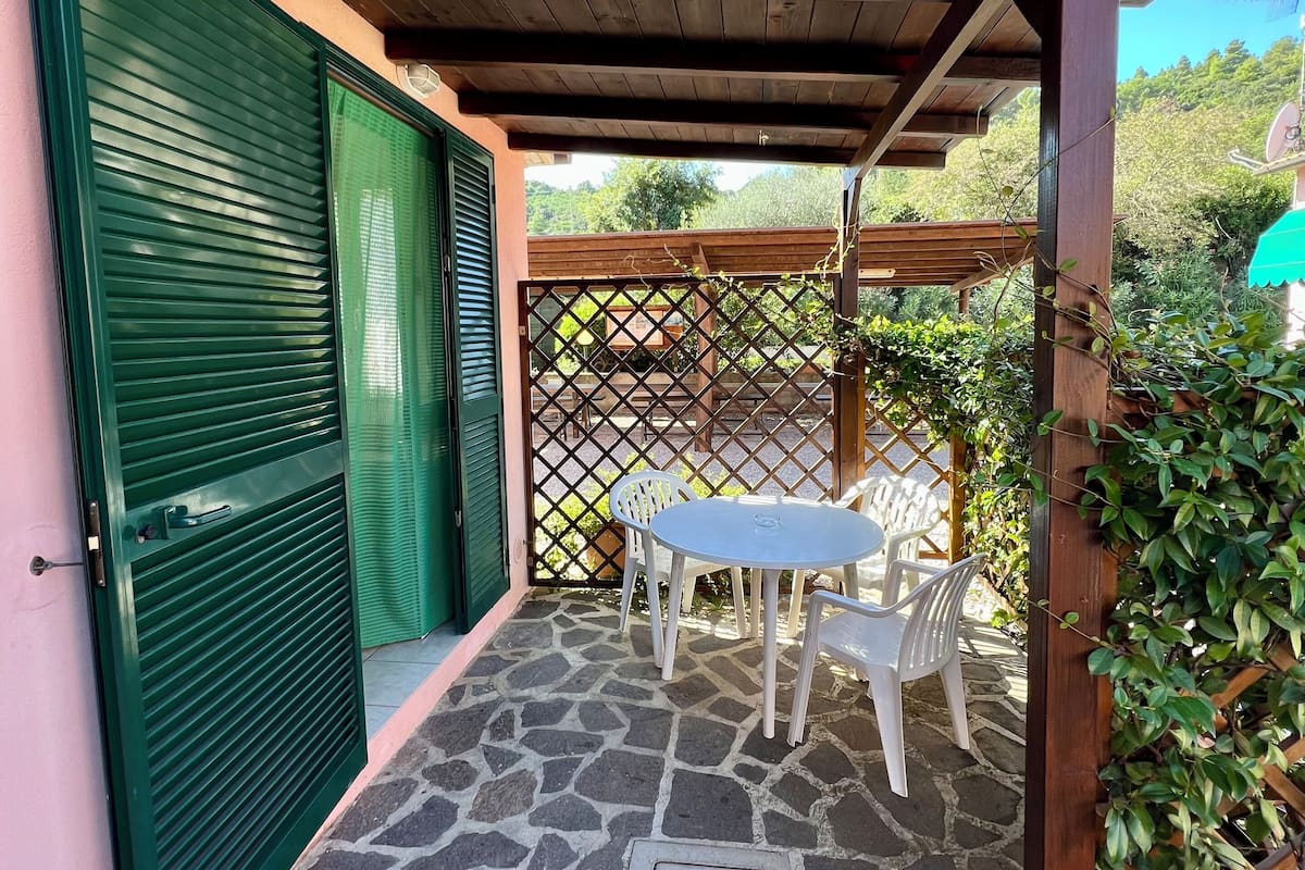 A covered patio with a stone floor, a table with chairs, and a green door.