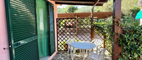 A covered patio with a stone floor, a table with chairs, and a green door.