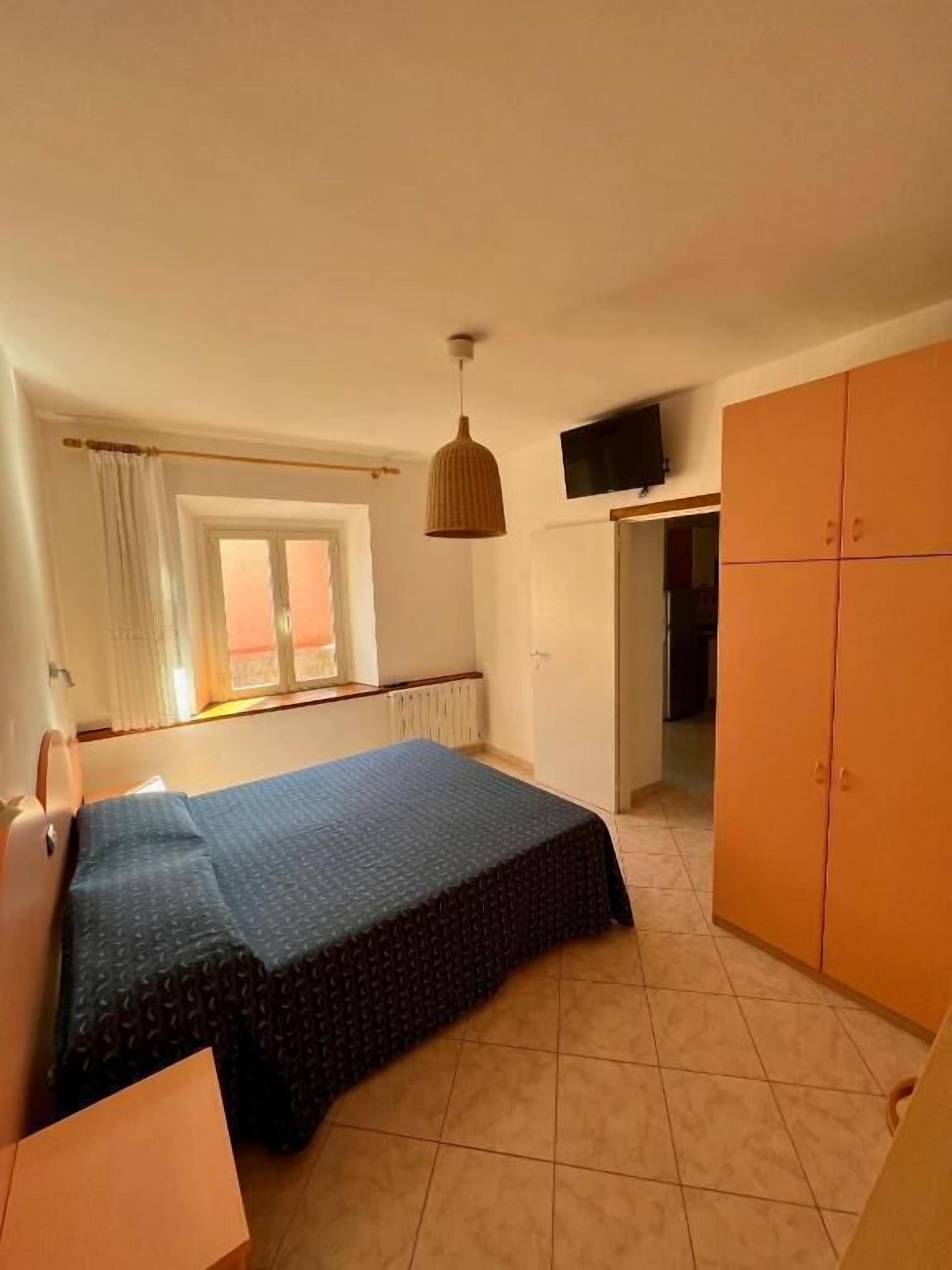 Quarto com cama, guarda-roupa, televisão na parede e janela com cortinas.