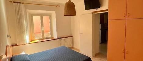 Quarto com cama, guarda-roupa, televisão na parede e janela com cortinas.