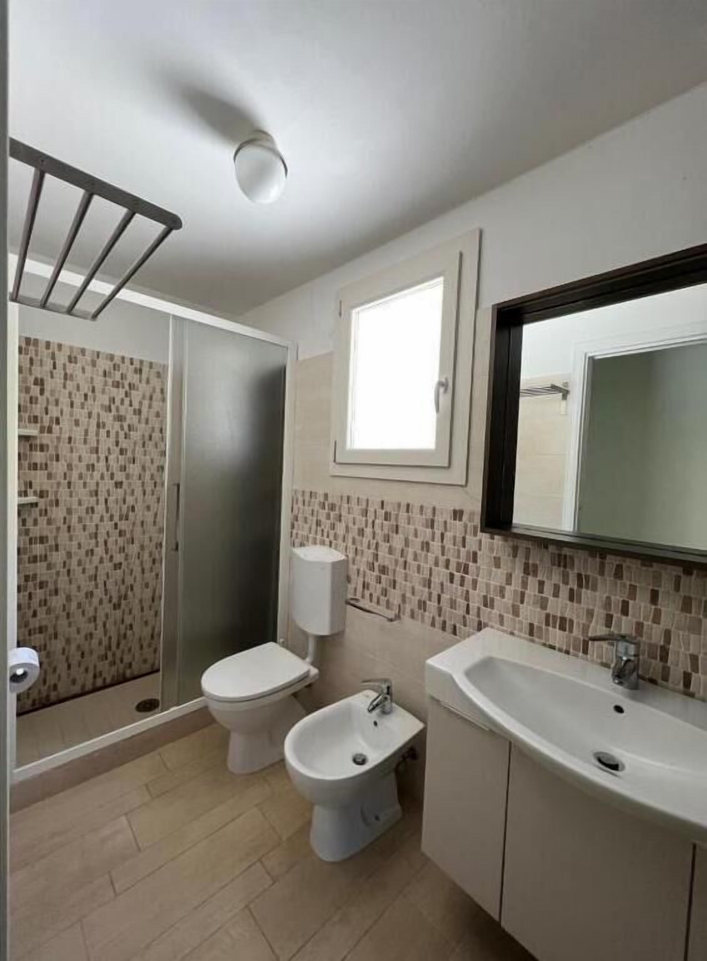 A bathroom with a shower, toilet, bidet, and sink.