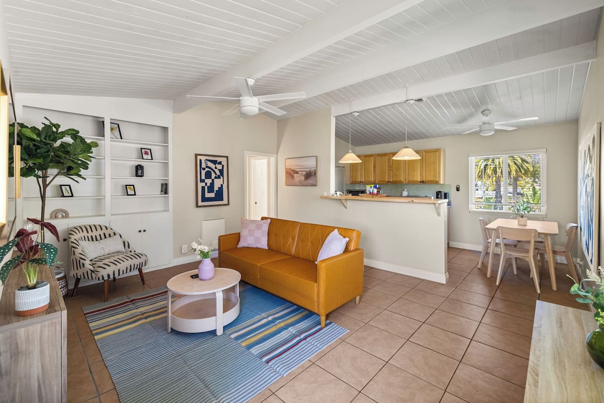 A spacious living area with a sofa, armchair, and coffee table, connected to a kitchen with wooden cabinets and a dining area.