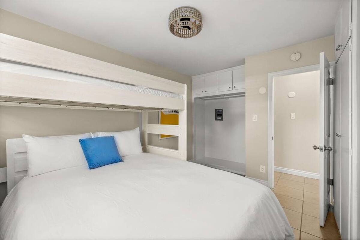 A hotel room with a bunk bed, a minibar, a refrigerator, and a door leading to another room.