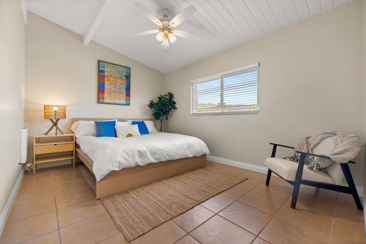 A bedroom with a bed, a nightstand, a chair, a window, and a ceiling fan.