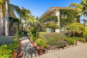 A residential building with a covered outdoor staircase, lush garden, and palm trees. - Los Aguajes (Santa Barbara)