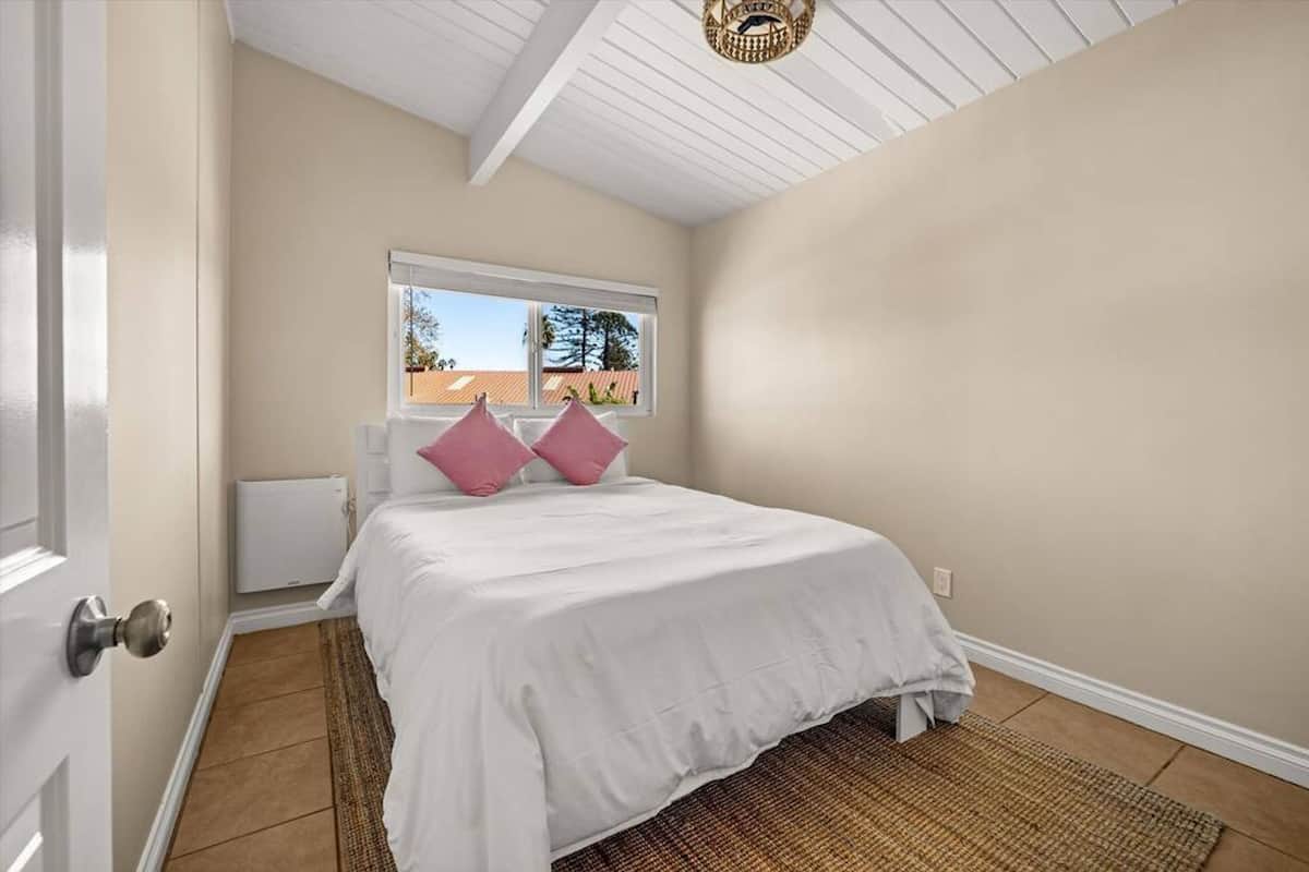 A bedroom with a bed, two pink pillows, a window, a radiator, and a ceiling fan.