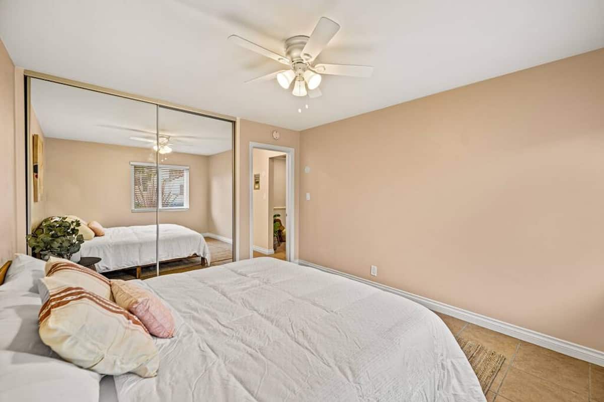 A bedroom with a large mirror, a ceiling fan, and a bed with white bedding.