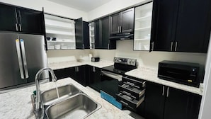 A modern kitchen with black cabinets, stainless steel appliances, and a granite countertop. - Spacious & Modern 4 BR House (Brantford)