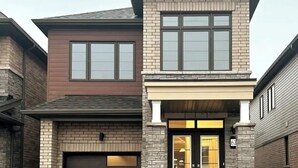 A two-story residential building with a garage door, a front entrance with glass doors, and a brick facade. - Spacious & Modern 4 BR House (Brantford)