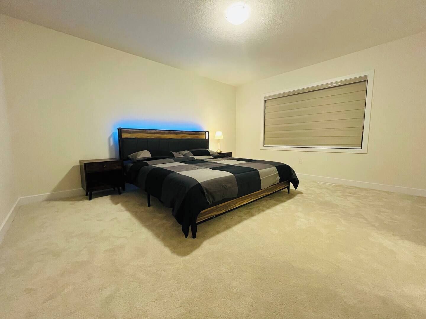 A bedroom with a bed, nightstands, a lamp, and a window with blinds.