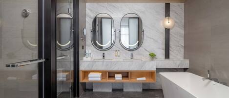 A modern bathroom with a glass shower enclosure, a freestanding bathtub, and a vanity with two sinks and a mirror.