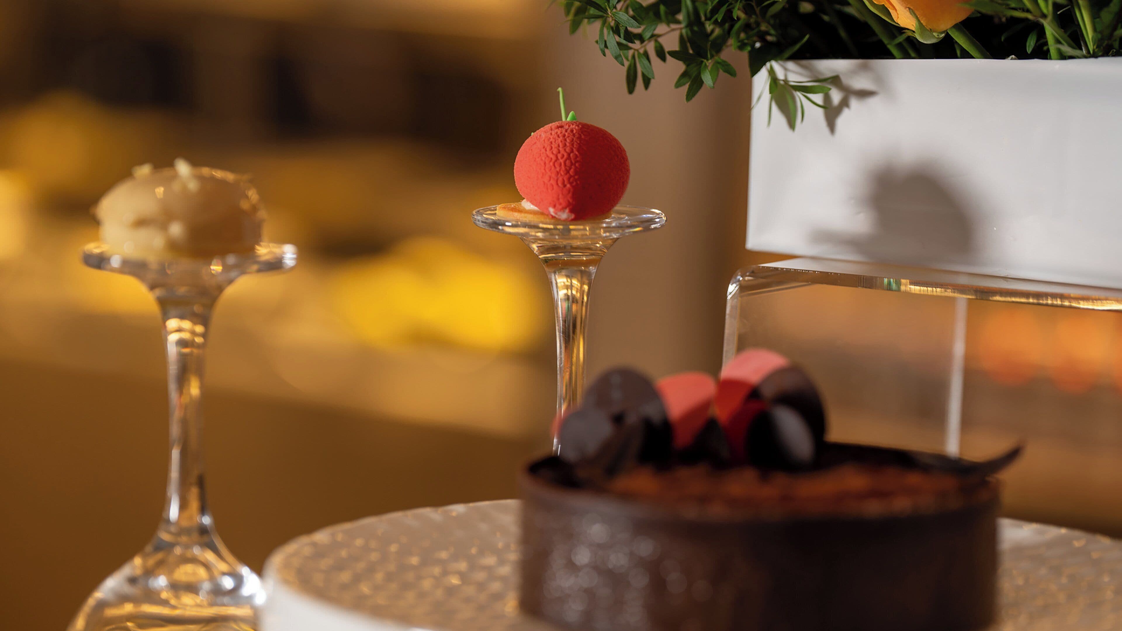 A dessert display with a chocolate cake and a strawberry on a glass stand.