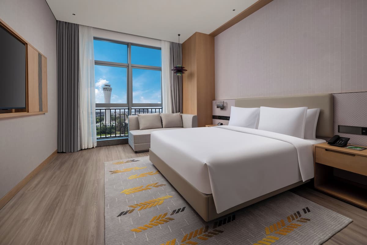 Une chambre d’hôtel avec un grand lit, une table de chevet avec un téléphone, une commode, une fenêtre avec des rideaux et une vue sur une tour.