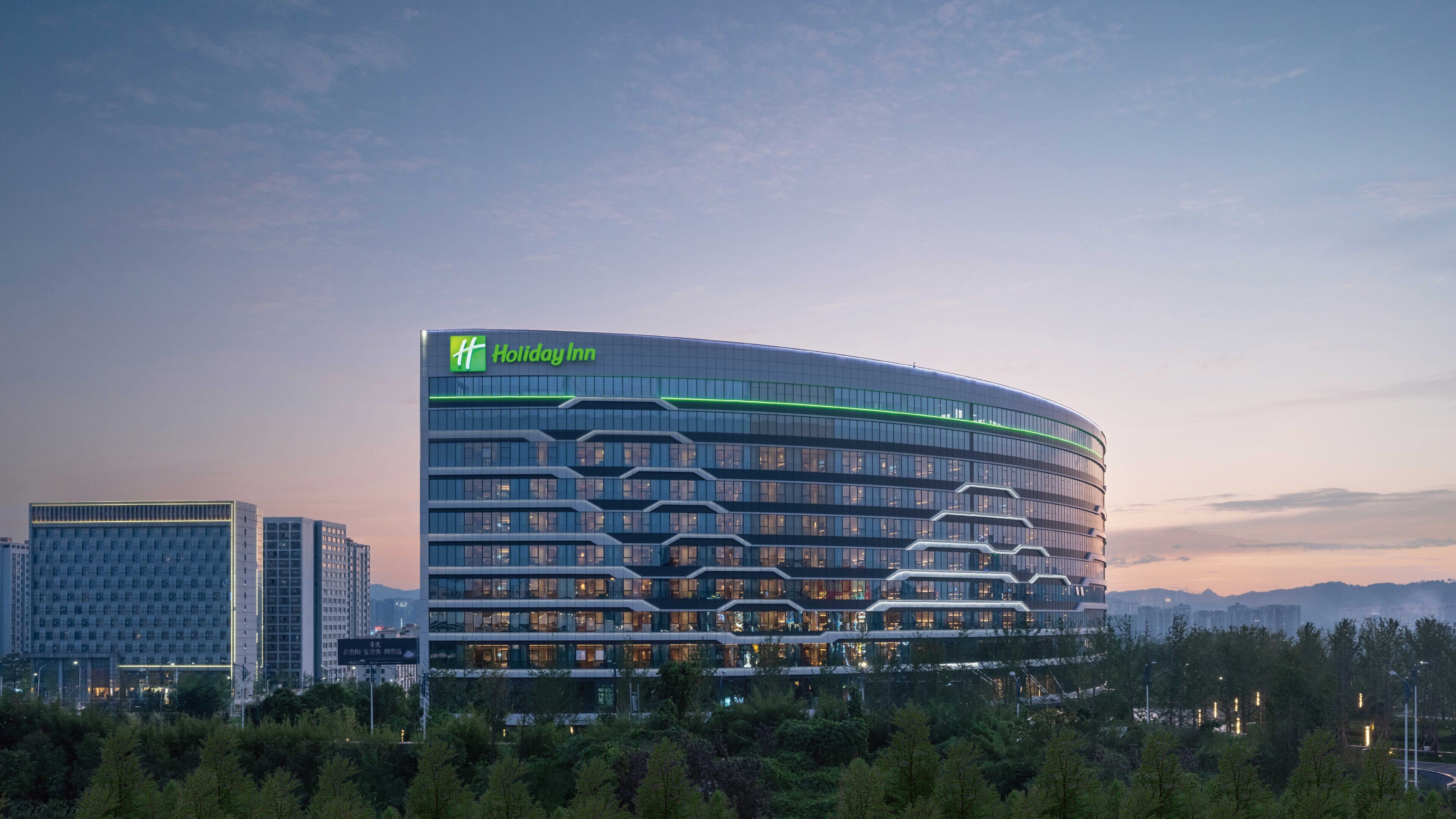 Un hotel moderno Holiday Inn con fachada curva, varios pisos y un logotipo verde destacado.