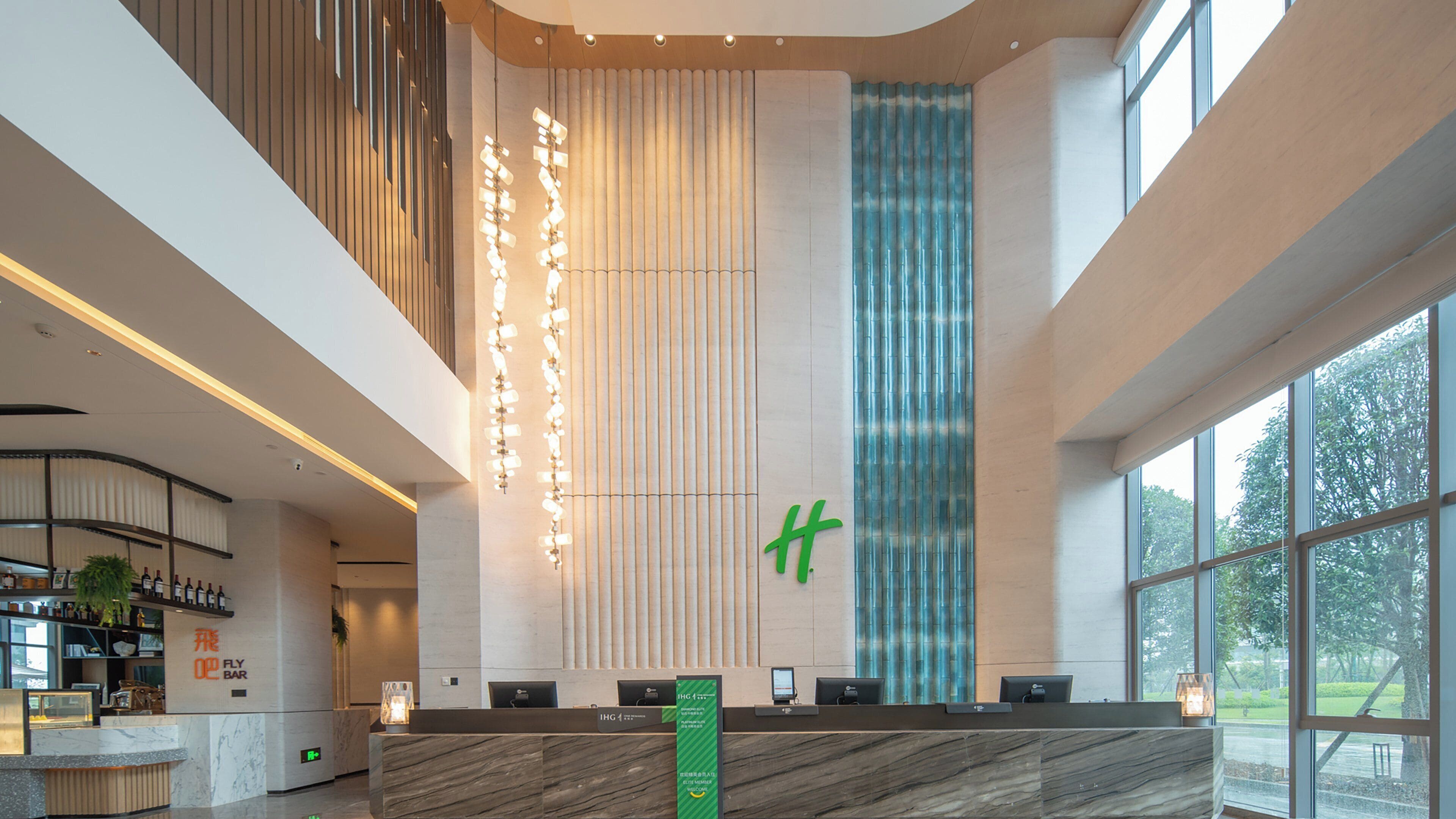 Una moderna zona de recepción de hotel con mostrador de mármol, una instalación de luces verticales y un amplio ventanal con vistas al exterior.